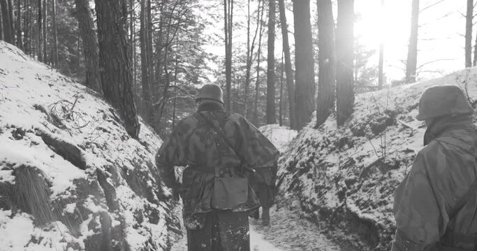 Re-enactors Dressed As German Infantry Soldier Marching Through Forest Road In Winter Day. Group Of Soldiers Sub-machine Guns And Bazooka Marching In Forest. Wehrmacht Army Soldiers Of World War Ii.