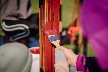 Valmiera, Latvia - April 21, 2024 - A close-up of a hand applying red paint to a wooden beam with a...