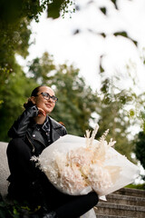 Young pretty girl is holding a huge bouquet of white hydrangeas and white roses on her lap, sitting...
