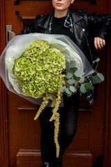 Large bouquet of green hydrangeas wrapped in transparent and white paper in a woman's hands