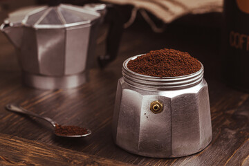 Moka coffee pot filled with brown ground coffee on dark wooden board, prepare to brewing Italian espresso.