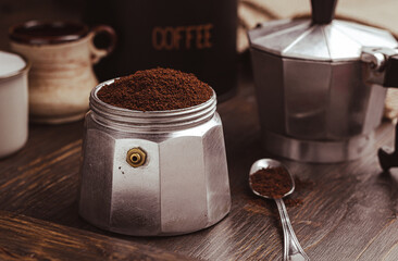 Moka coffee pot filled with brown ground coffee on dark wooden board, prepare to brewing Italian espresso.