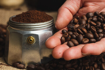 Hands holding roasted coffee beans on burlap and coffee background. Focus on beans. Close up.
