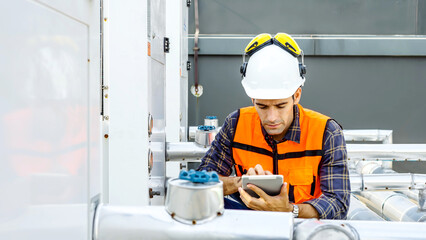 Male technical foreman in safety uniform inspects maintenance work holding a tablet to look at...