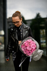 Young pretty woman wearing glasses holding a bouquet of pink roses