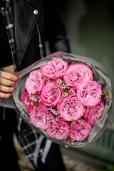 Close up of a bouquet of pink roses with tiny daisies, wrapped in gray wrapping paper