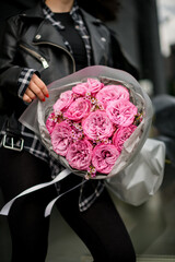 Close-up of a bouquet of pink roses with tiny daisies, wrapped in gray wrapping paper, which female hands carefully unfold