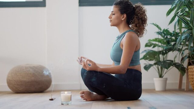 Video of sporty young woman doing yoga and hypopressive exercises while staying in lotus position in living room at home.
