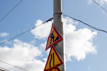 Three street signs on a pole against a blue sky with overhead power lines