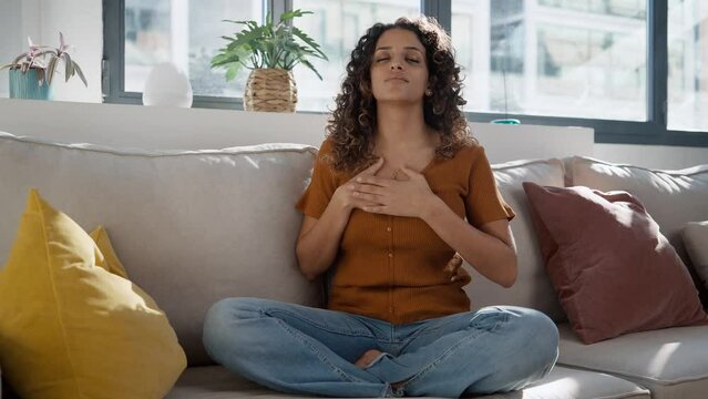 Video of  pretty young woman in lotus position sitting on the sofa at living room at home.