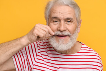 Senior man touching mustache on orange background