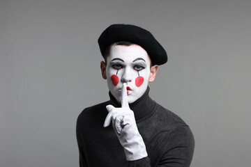 Mime artist in beret showing hush gesture on grey background