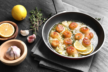 Delicious scallops with sauce in frying pan and ingredients on dark gray textured table, closeup