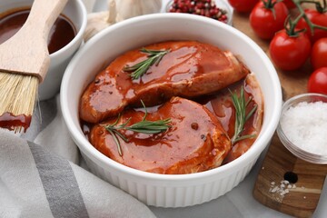 Raw marinated meat and rosemary in bowl on table, closeup