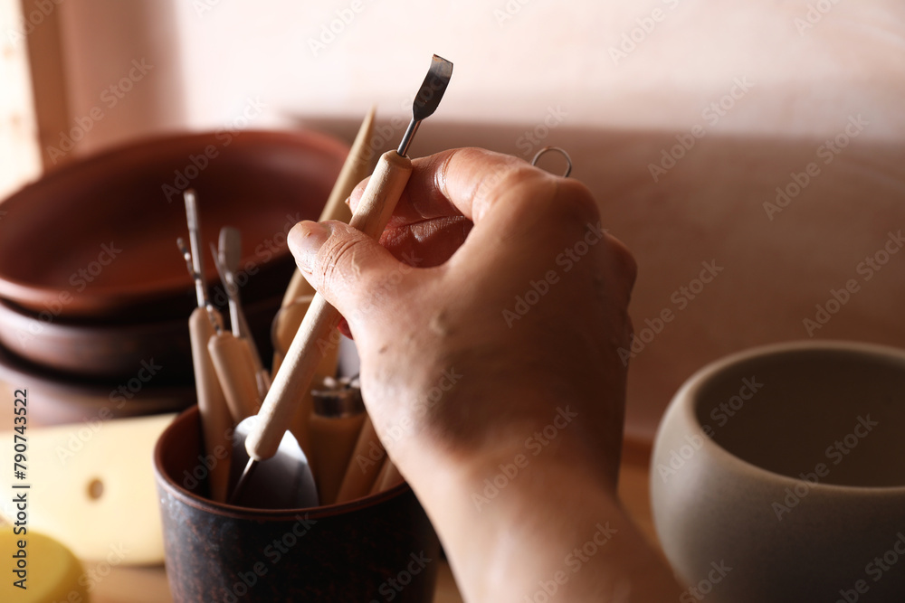 Wall mural Woman taking clay crafting tool from cup in workshop, closeup