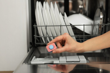 Woman putting detergent tablet into open dishwasher, closeup