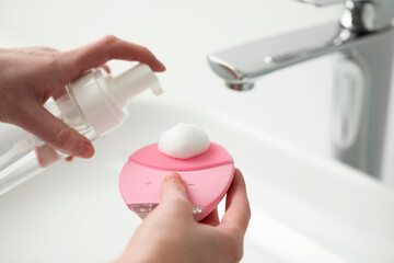Washing face. Woman applying cleansing foam onto brush above sink in bathroom, closeup