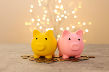Piggy banks and coins on grey table against blurred lights