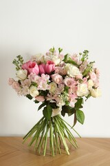 Beautiful bouquet of fresh flowers on wooden table near white wall