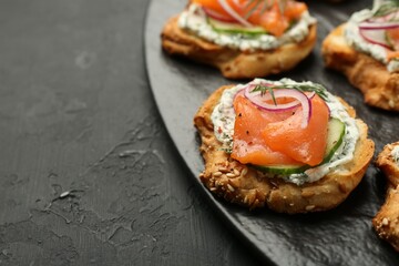Tasty canapes with salmon, cucumber, radish and cream cheese on black table, closeup. Space for text