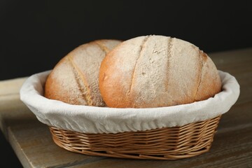 Wicker basket with fresh bread on wooden table, closeup