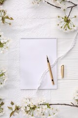 Guest list. Notebook, pen, spring tree branches with beautiful blossoms and lace ribbons on white wooden background, flat lay