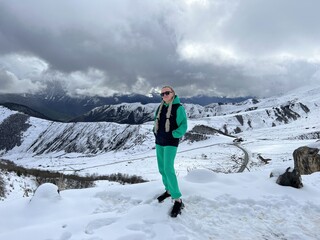 A woman on the background of the Ceylomsky pass in Ingushetia. A trip uphill to the Tsei Lum pass on a cloudy spring day. Panorama of the high cliffs of the Dzheyrakh gorge