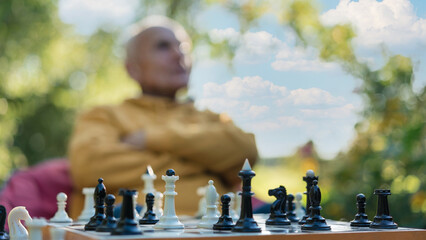 Blurred senior man contemplating next move in chess game outdoors. Strategy and concentration in serene park setting