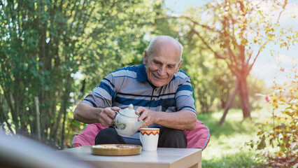 Senior man pours tea outdoors smiling in lush garden evoking sense of calm and relaxation. Simple joys and serene nature embrace during peaceful break