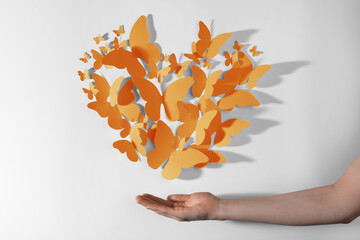 Orange paper butterflies on white wall. Woman showing decorative element