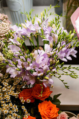 Sprigs of purple freesia next to tiny daisies, roses and other decorative elements of the florist