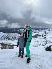 A woman with a child on the background of the Ceylomsky pass in Ingushetia. A trip uphill to the Tsei Lum pass on a cloudy spring day. Panorama of the high cliffs of the Dzheyrakh gorge