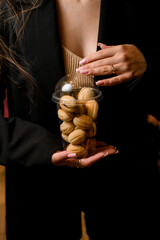 Female hands hold a transparent plastic cup with baked sweet nuts with filling