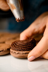 Female hands of a confectioner squeeze chocolate cream from a pastry bag through a shaped nozzle