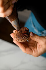 Top view of female hands of a confectioner squeezing chocolate cream from a pastry bag through a shaped nozzle