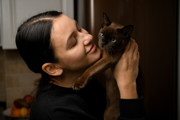 Cute smiling young woman holding and hugging a small black kitten