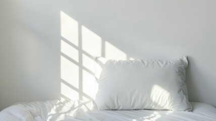 White pillow and bedding in sunlight with window shadow pattern on wall