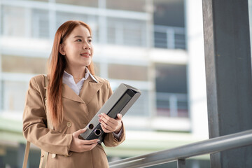 Happy young Asian female businesswoman using cell phone smartphone and holding document files phone at the walkway