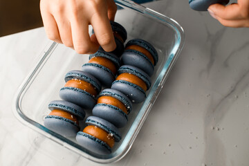 Female hands of a confectioner put blue macaroons with chocolate cream into a glass
