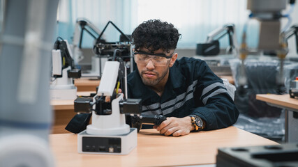 Engineering student assembling a robotic arm using a computer in a technology workshop. Service engineer holding a robot controller and inspecting the robotic arm's welding hardware.