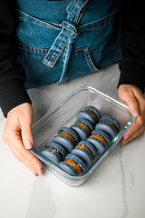 Female hands hold a glass container containing blue macaroons with chocolate cream