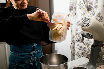 Smiling woman confectioner pours beige cream into the bowl of a stationary mixer