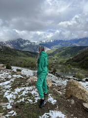Naklejka premium A woman on the background of the Ceylomsky pass in Ingushetia. A trip uphill to the Tsei Lum pass on a cloudy spring day. Panorama of the high cliffs of the Dzheyrakh gorge