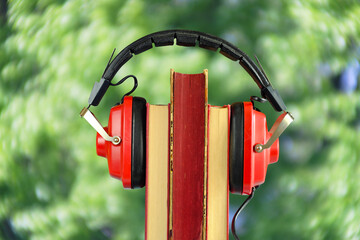 New audiobook releases for spring and summer holiday read  and listening  with row of books ang vintage headphone,blurred swirly nature background.Vacation,inspiration,relaxation,literature concept.