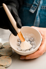 Woman's hand holds a ceramic bowl with nuts sprinkled with silver paint, the other hand holds a brush