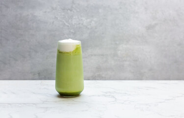 Matcha latte green tea with milk foam in tall glass isolated on grey background, copy space.