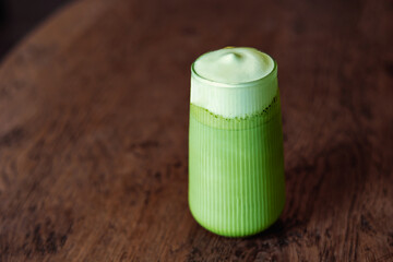 Matcha latte green tea with milk foam in tall glass isolated on dark wooden table background, copy space.