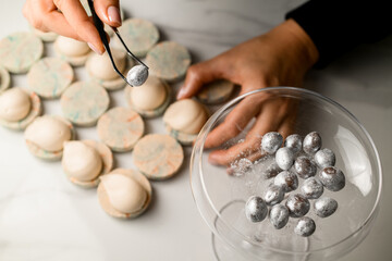 Confectioner's female hands hold tweezers with a silver nut and half of a macaron with cream