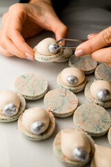 Female hands of a confectioner decorate the last white macaron with a silver nut, like a pearl