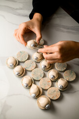 Top view of confectioner's female hands decorating the last white macaron with a silver nut like a pearl